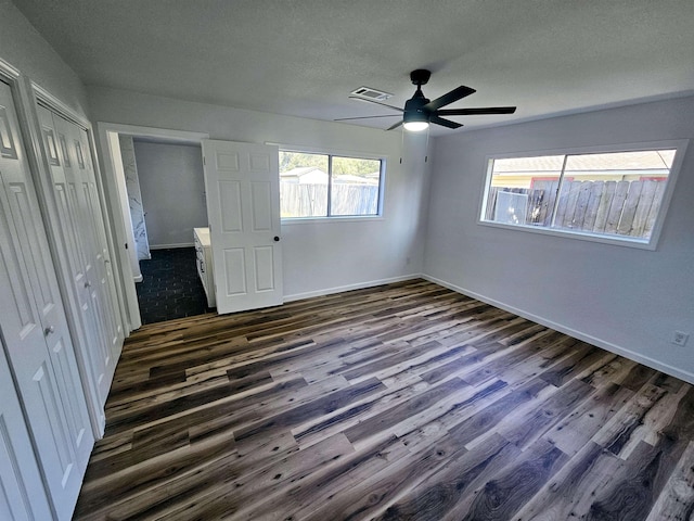 unfurnished bedroom with multiple closets, ceiling fan, dark wood-type flooring, and a textured ceiling