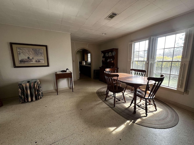 dining room featuring arched walkways, speckled floor, visible vents, and baseboards