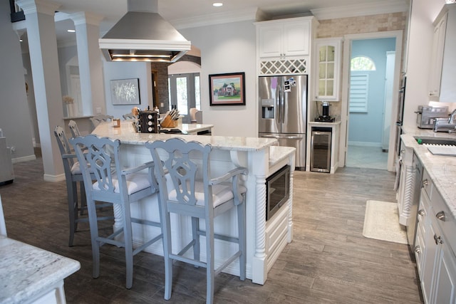 5065 Oakmont Dr, Beaumont, TX 77706 - kitchen with appliances with stainless steel finishes, wine cooler, island exhaust hood, a kitchen bar, and white cabinetry