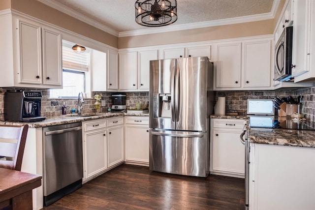 kitchen with stainless steel appliances, white cabinetry, sink, and dark stone countertops