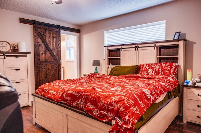 bedroom featuring ceiling fan, a barn door, dark hardwood / wood-style floors, and a textured ceiling