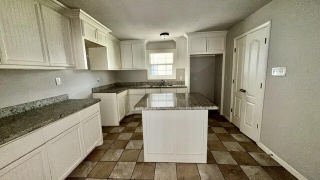 5440 Margo Ln, Beaumont, TX 77708 - kitchen featuring white cabinetry, baseboards, a kitchen island, a sink, and stone countertops