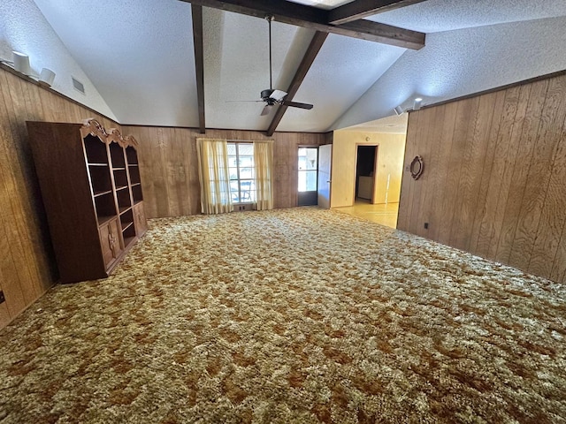 carpeted empty room with wood walls, ceiling fan, lofted ceiling with beams, and a textured ceiling