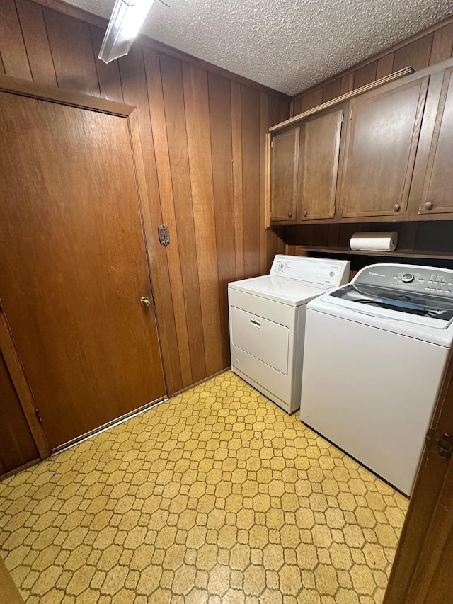 washroom featuring cabinets, separate washer and dryer, a textured ceiling, and wooden walls