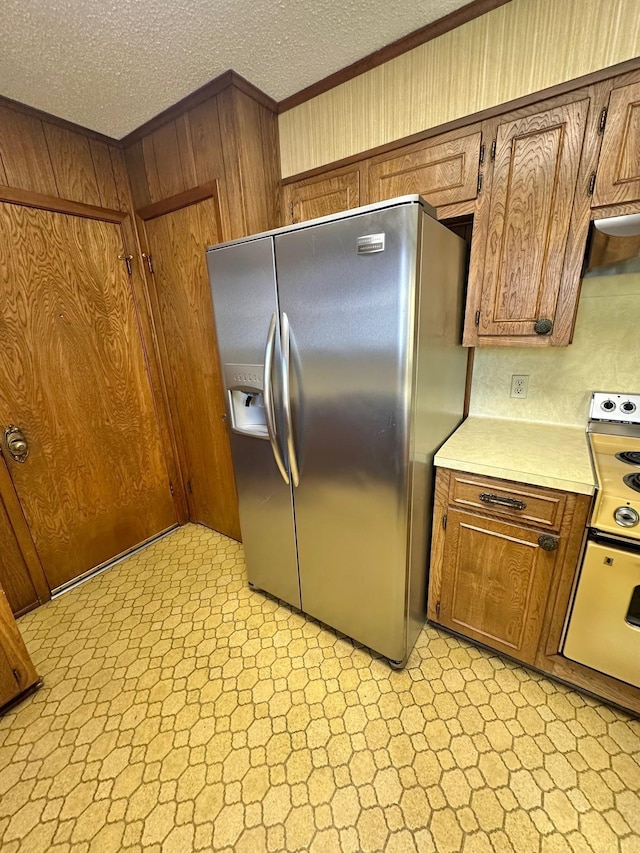 kitchen with stainless steel refrigerator with ice dispenser, a textured ceiling, white electric range, and wood walls