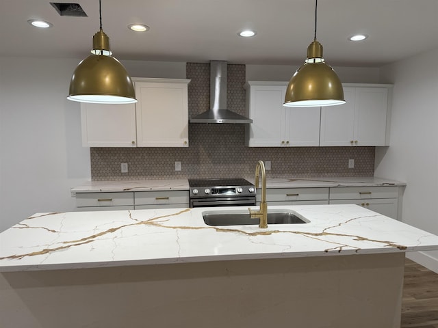 kitchen with wall chimney exhaust hood, light stone countertops, a center island with sink, and white cabinets