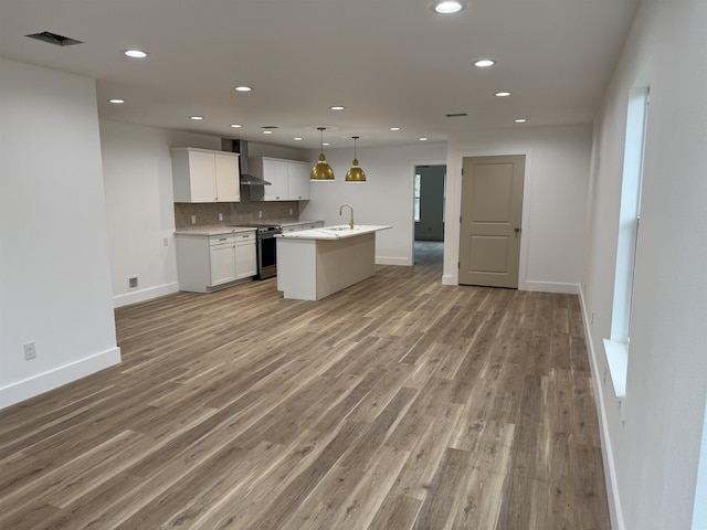 kitchen featuring wall chimney range hood, a center island with sink, decorative light fixtures, white cabinetry, and stainless steel range with electric cooktop