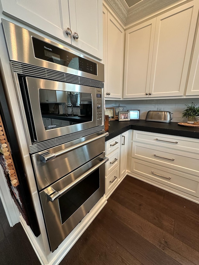 kitchen with white cabinetry, stainless steel double oven, and dark hardwood / wood-style floors