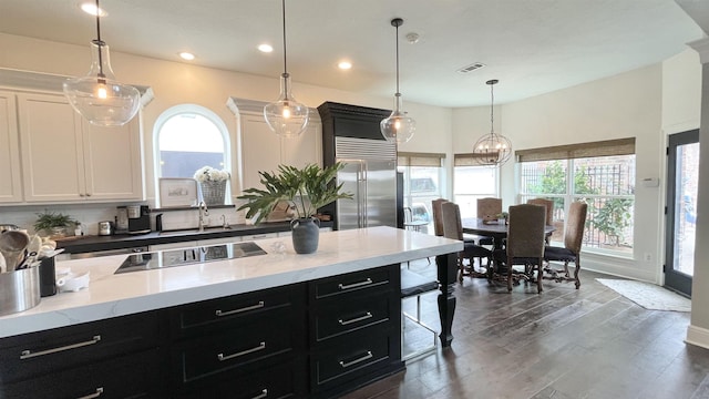 kitchen with built in fridge, white cabinetry, black electric cooktop, and decorative light fixtures