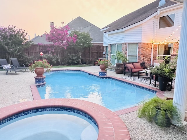 pool at dusk featuring a patio area and an in ground hot tub