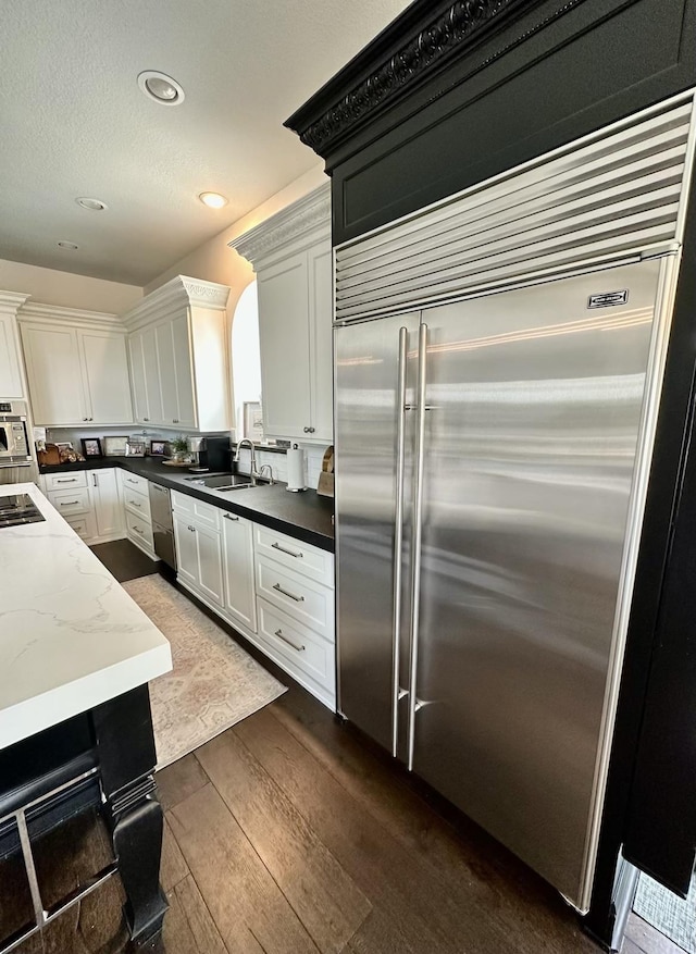 kitchen with sink, dark wood-type flooring, appliances with stainless steel finishes, dark stone countertops, and white cabinets