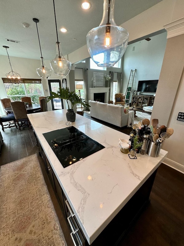 kitchen with a center island, light stone countertops, hanging light fixtures, and black stovetop