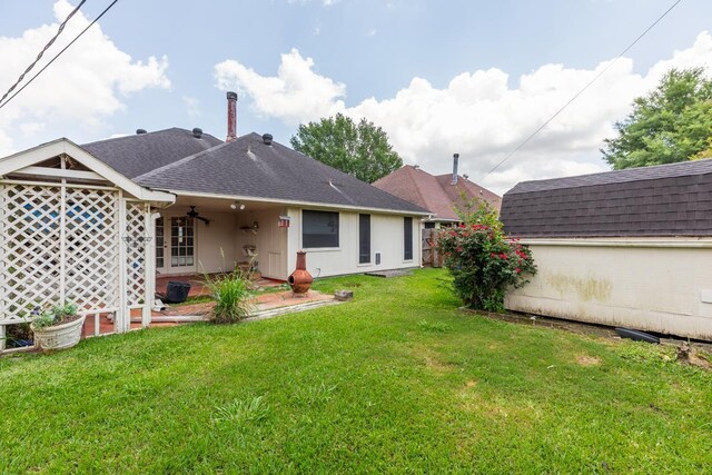 rear view of house with an outbuilding, a yard, a shingled roof, and a patio area