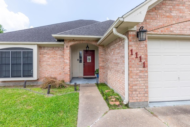 entrance to property featuring a lawn, roof with shingles, brick siding, and a garage