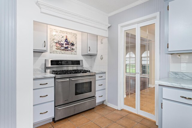 kitchen with backsplash, white cabinets, stainless steel gas range, light tile patterned floors, and ornamental molding