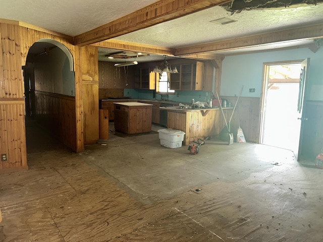 kitchen with glass insert cabinets, a center island, wood walls, decorative light fixtures, and arched walkways