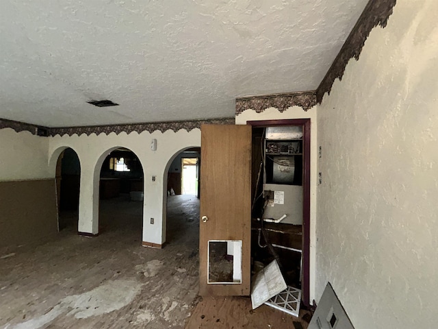 spare room with arched walkways, a textured wall, and a textured ceiling