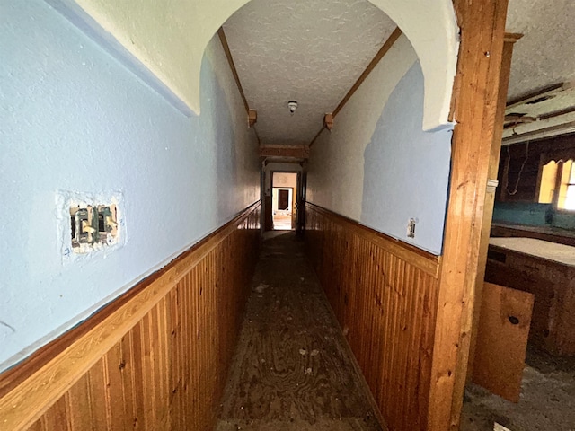 corridor with wood walls, arched walkways, and wainscoting