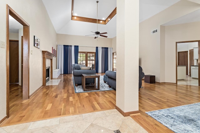 living room with ceiling fan, a fireplace, light tile patterned flooring, and a high ceiling