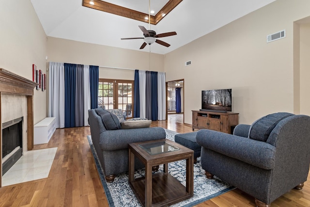 living room with hardwood / wood-style floors, ceiling fan, a towering ceiling, and a tile fireplace