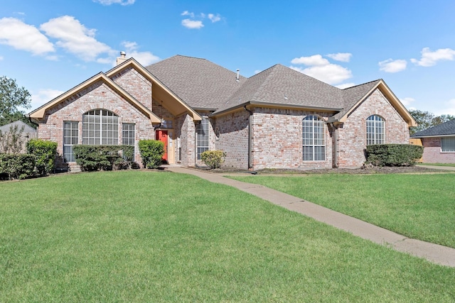 french provincial home with a chimney, brick siding, roof with shingles, and a front yard