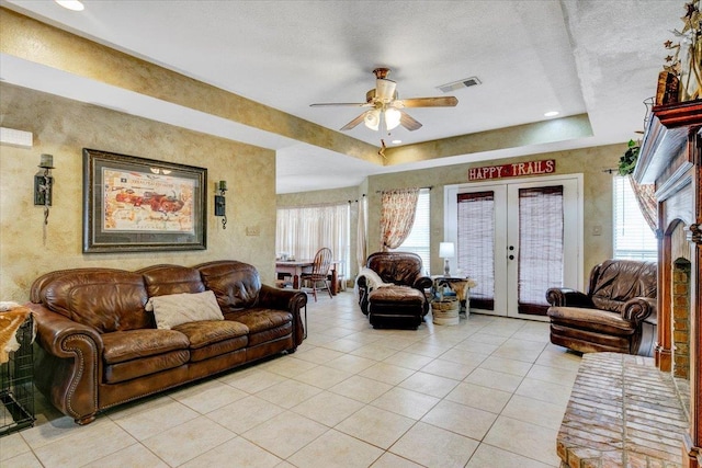 living room featuring ceiling fan, french doors, a raised ceiling, a textured ceiling, and light tile patterned flooring