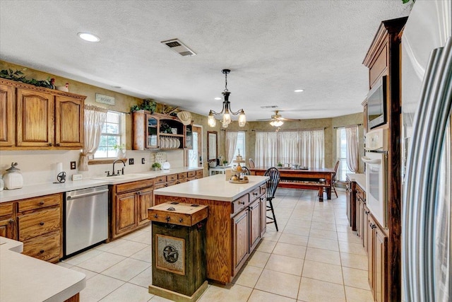 kitchen featuring ceiling fan with notable chandelier, sink, decorative light fixtures, a kitchen island, and stainless steel appliances