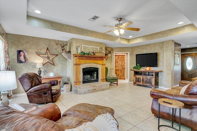 tiled living room featuring a raised ceiling, ceiling fan, and a brick fireplace