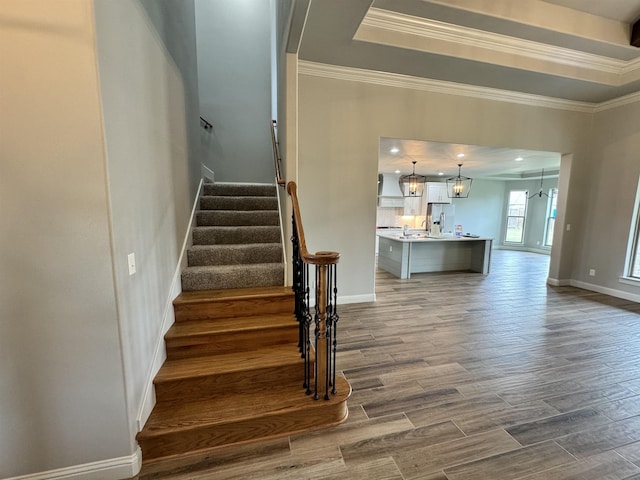 stairs with a tray ceiling, crown molding, and a notable chandelier