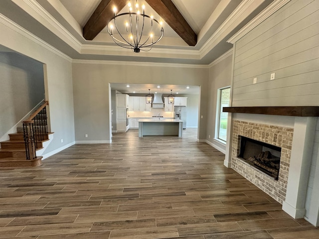 unfurnished living room featuring beamed ceiling, a high ceiling, a notable chandelier, and ornamental molding