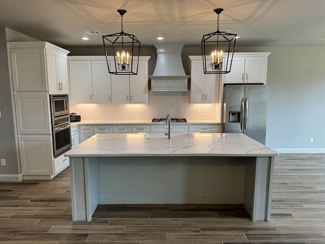 kitchen with stainless steel appliances, pendant lighting, a kitchen island with sink, white cabinets, and custom exhaust hood