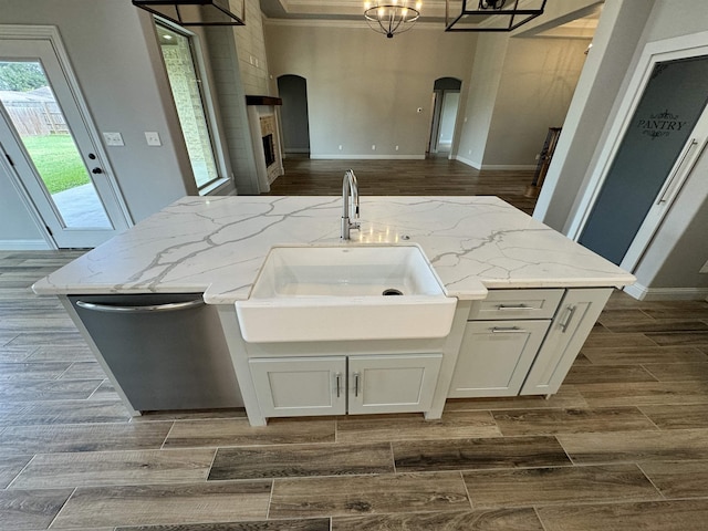 kitchen featuring light stone countertops, sink, stainless steel dishwasher, an island with sink, and a fireplace