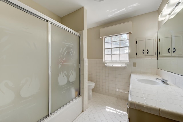 full bathroom featuring tile patterned flooring, combined bath / shower with glass door, toilet, vanity, and tile walls