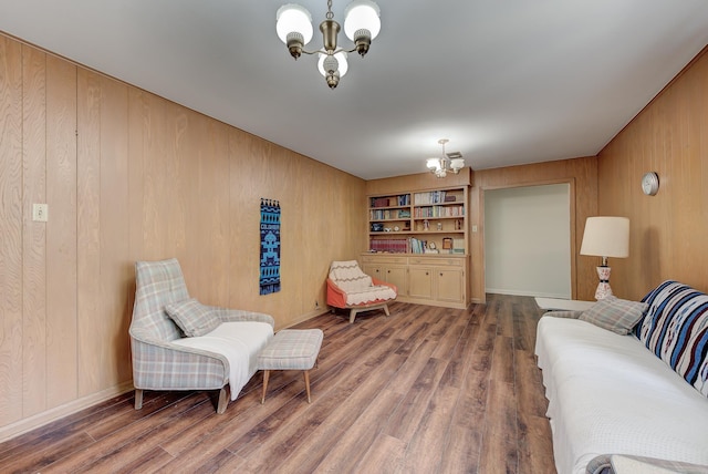 sitting room with built in shelves, wood-type flooring, wooden walls, and a chandelier