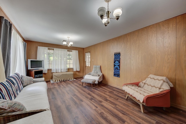 living room featuring dark wood-type flooring, wooden walls, and a chandelier