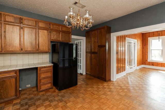 kitchen featuring black refrigerator, light parquet floors, tile counters, and a chandelier