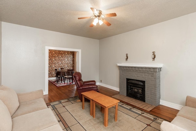 living room with a textured ceiling, a fireplace, ceiling fan, and light wood-type flooring