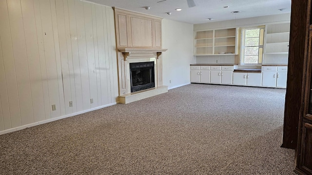 unfurnished living room with dark colored carpet, built in shelves, and wooden walls