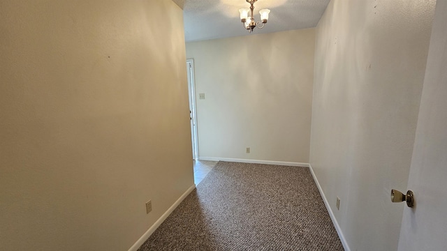 carpeted spare room featuring a textured ceiling and an inviting chandelier