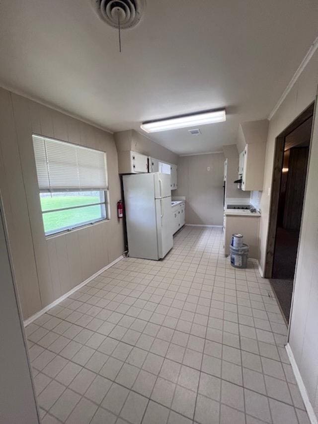 kitchen featuring white refrigerator, white cabinetry, crown molding, and light tile patterned flooring