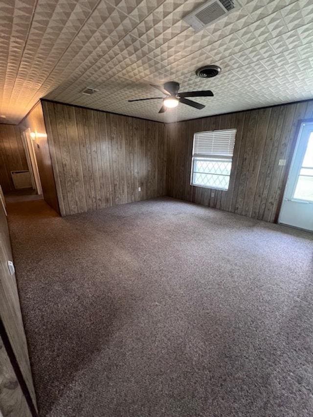 carpeted spare room with ceiling fan and wood walls