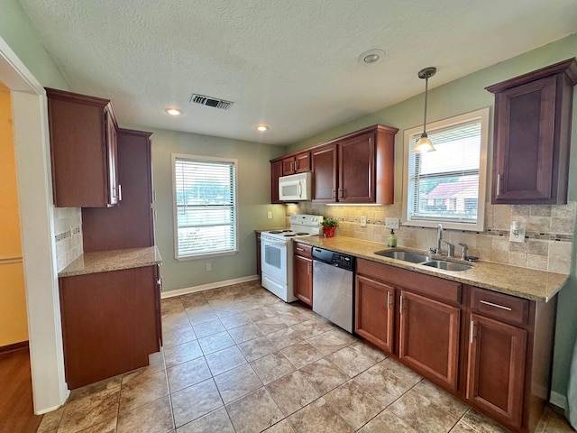 kitchen with decorative backsplash, white appliances, sink, light tile patterned floors, and hanging light fixtures