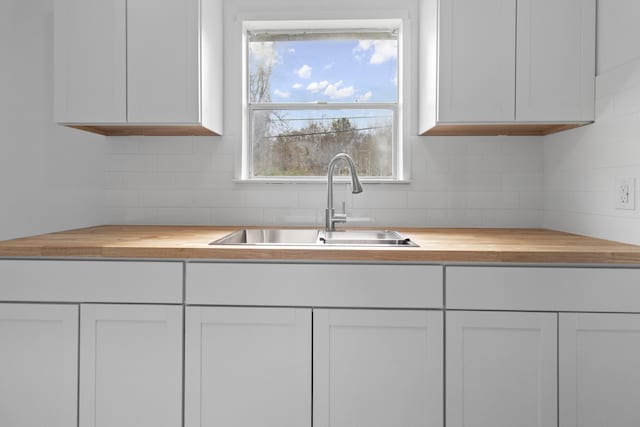 kitchen with sink, white cabinets, tasteful backsplash, and wood counters