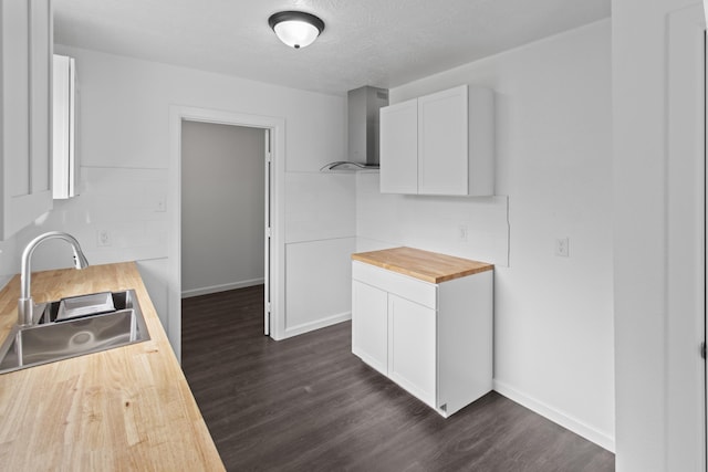 kitchen with sink, white cabinetry, butcher block countertops, dark hardwood / wood-style floors, and wall chimney range hood