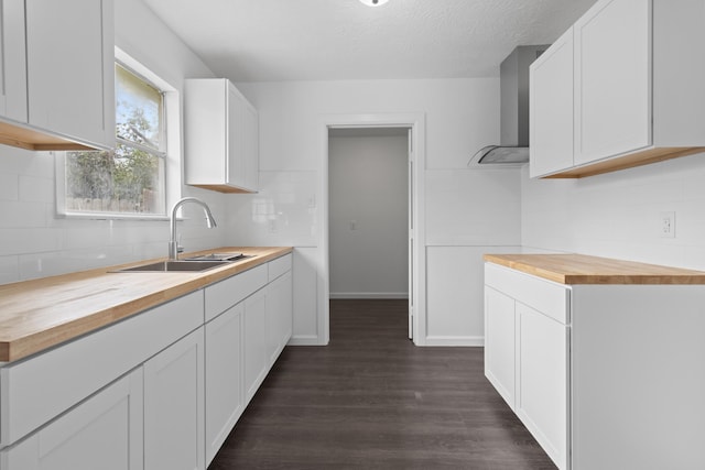 kitchen with wall chimney exhaust hood, dark hardwood / wood-style floors, wooden counters, white cabinetry, and sink