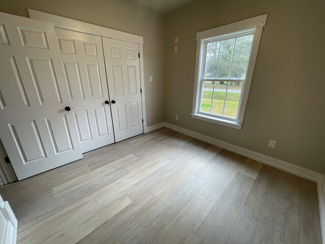 unfurnished bedroom featuring light wood-type flooring, baseboards, and a closet