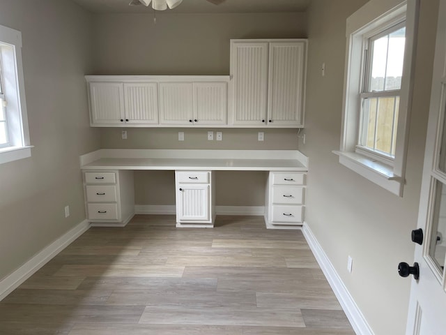 unfurnished office with baseboards, built in desk, and light wood-type flooring