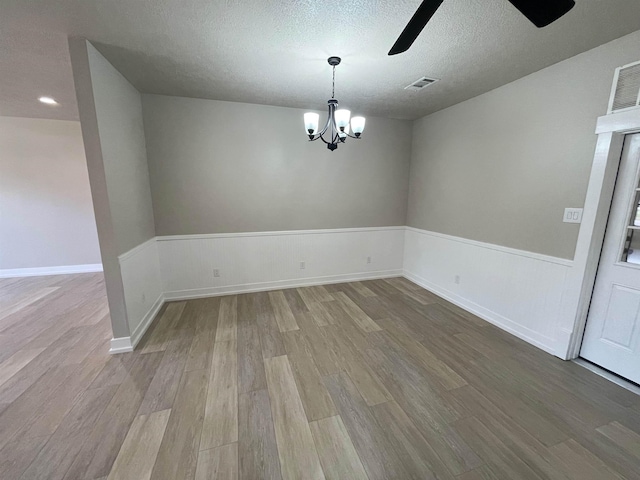 unfurnished dining area featuring wainscoting, wood finished floors, visible vents, and a textured ceiling