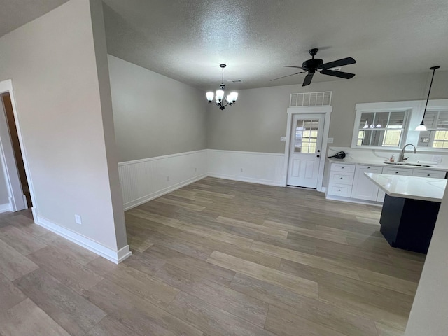 unfurnished dining area with visible vents, a wainscoted wall, a sink, a textured ceiling, and light wood-style floors