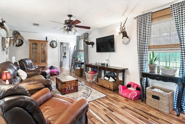 living room featuring wood-type flooring, a textured ceiling, and ceiling fan